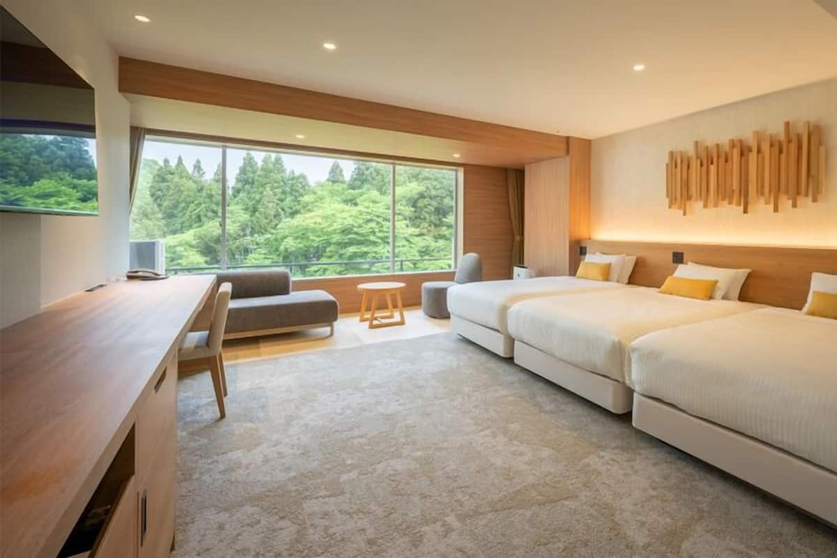 Ett modernt hotellrum med ett stort fönster, ett skrivbord, en soffa och två sängar.