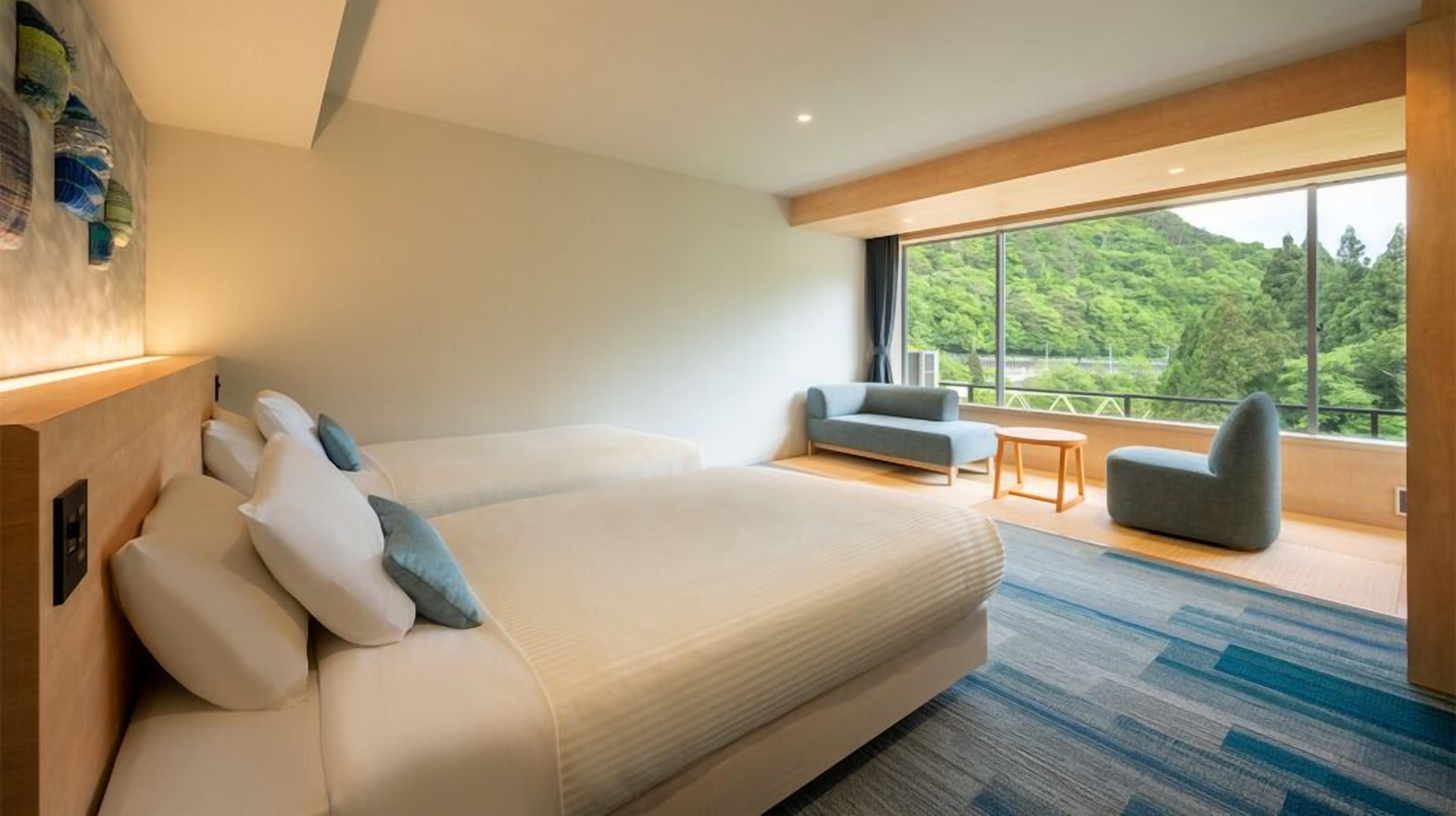 Een moderne hotelkamer met een groot bed, een bank, een kleine tafel en een balkon met uitzicht op groen.
