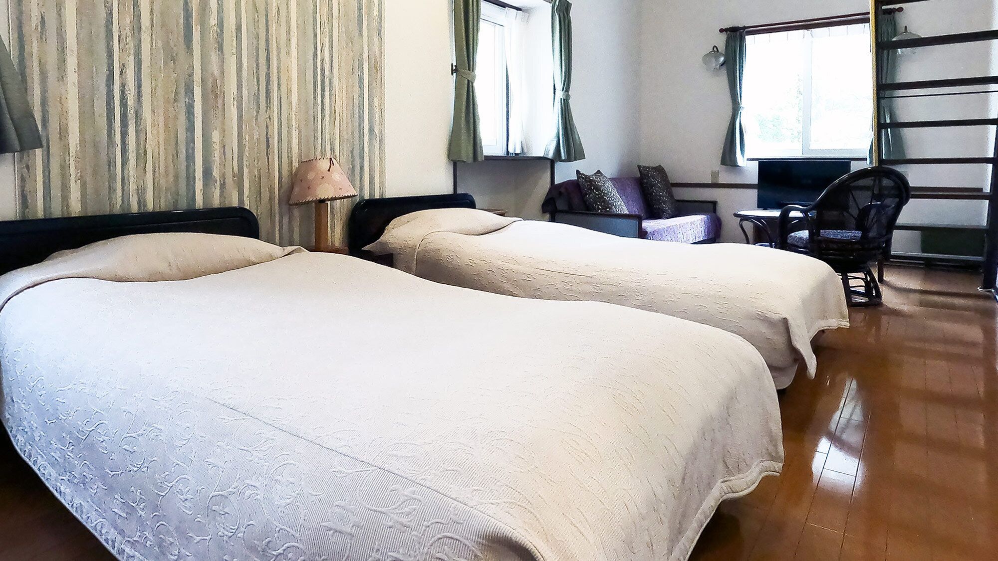 Una habitación con dos camas, una silla, una mesa y un ventanal con cortinas.