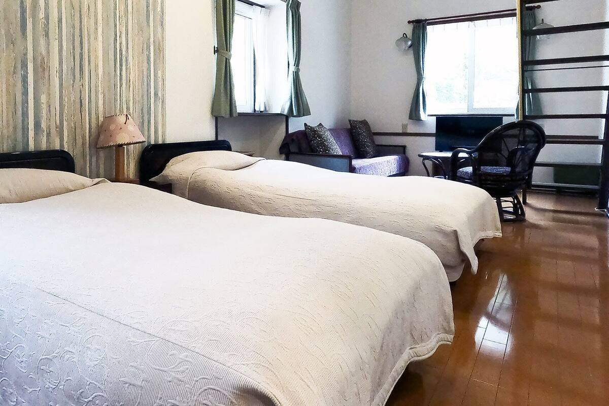A room with two beds, a chair, a table, and a window with curtains.