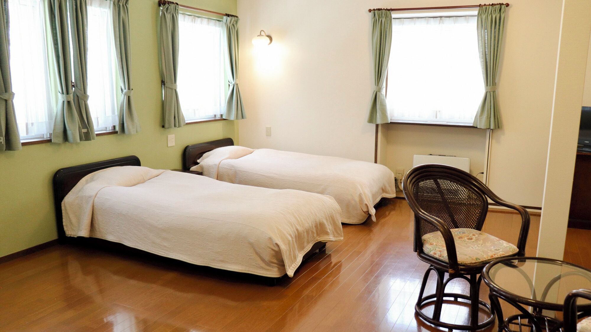 Una habitación con dos camas individuales, una silla, una mesa y una lámpara fijada a la pared.