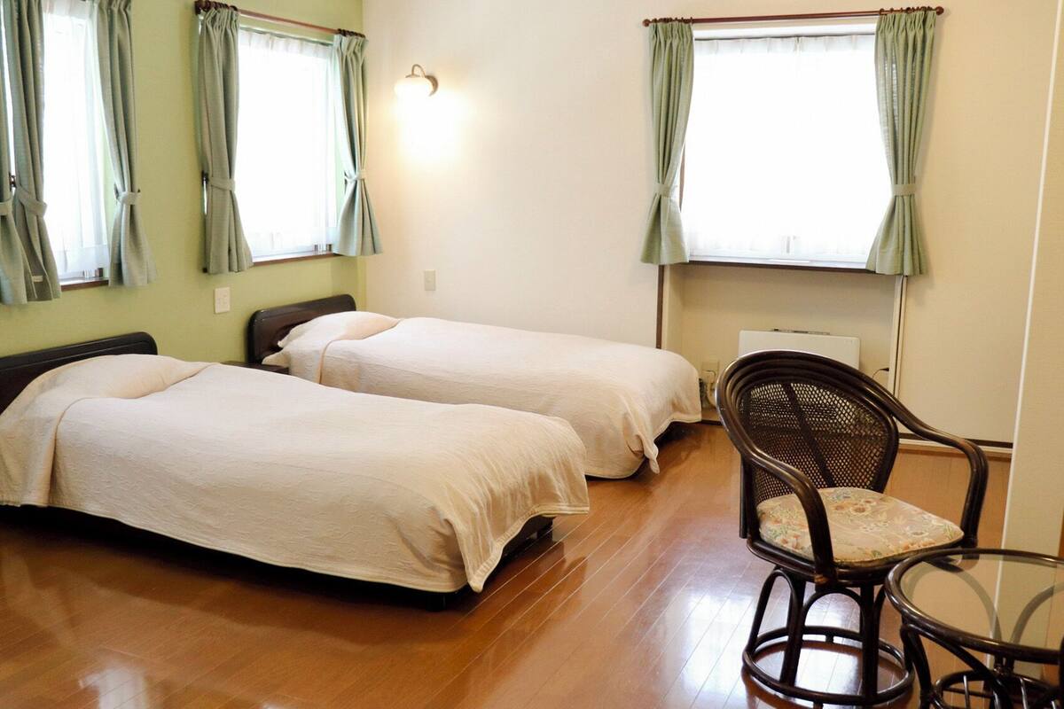 A room with two single beds, a chair, a table, and a wall-mounted light fixture.