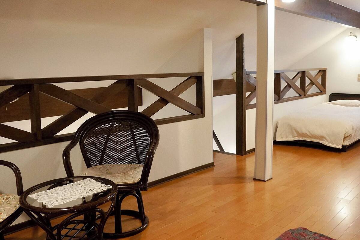 A room with a wooden floor, two beds, a chair, and a table.