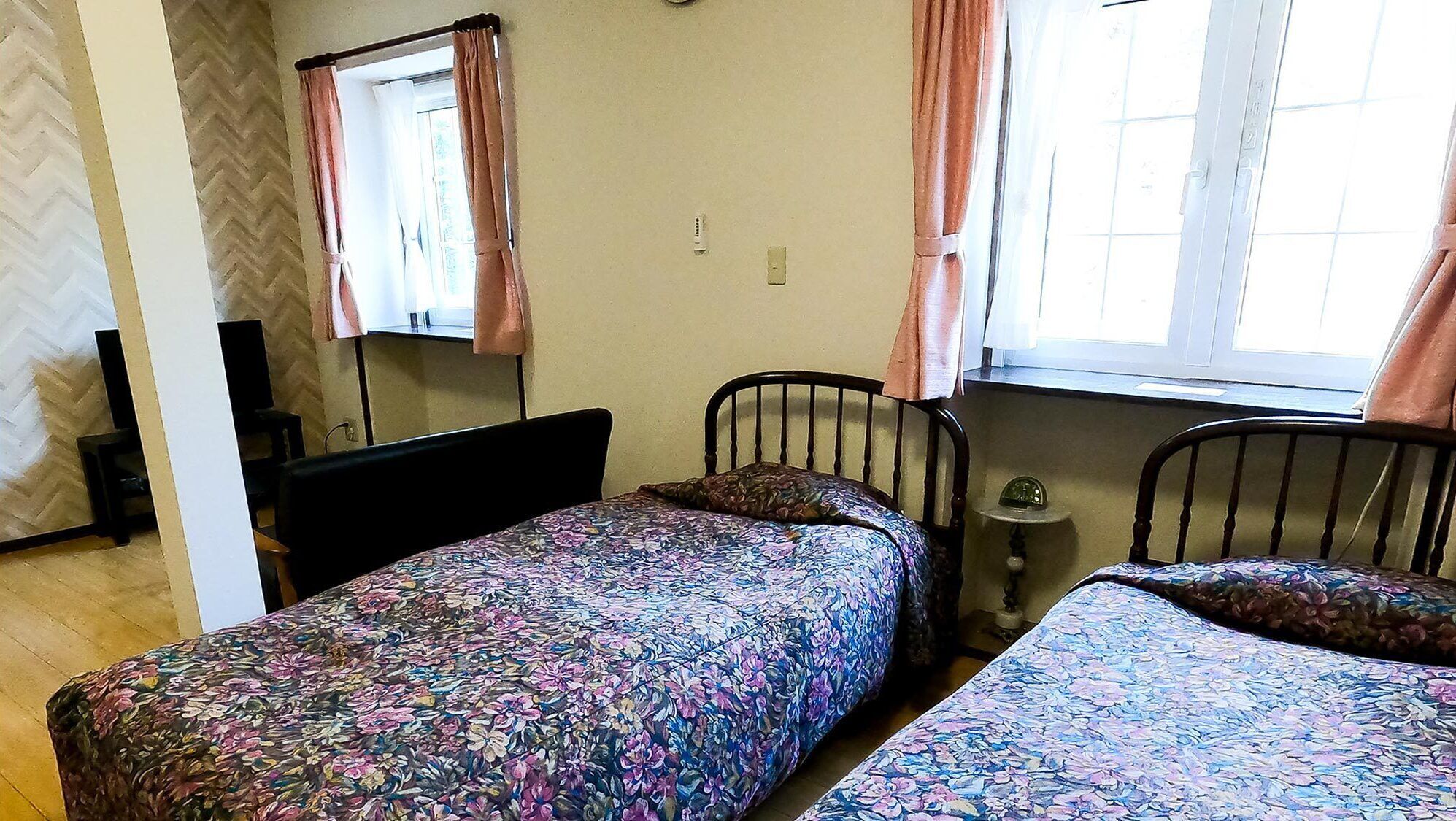 Una habitación con dos camas, una ventana con cortinas, un espejo y una mesita con un reloj.