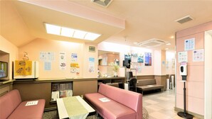 Un vestíbulo de hotel con zonas de estar, un mostrador de recepción y varios carteles informativos en las paredes.