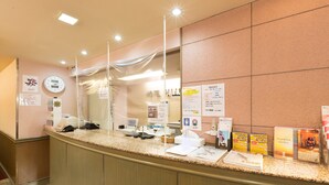 Mostrador de recepción de hotel con un reloj, carteles informativos y una barra con diversos objetos.