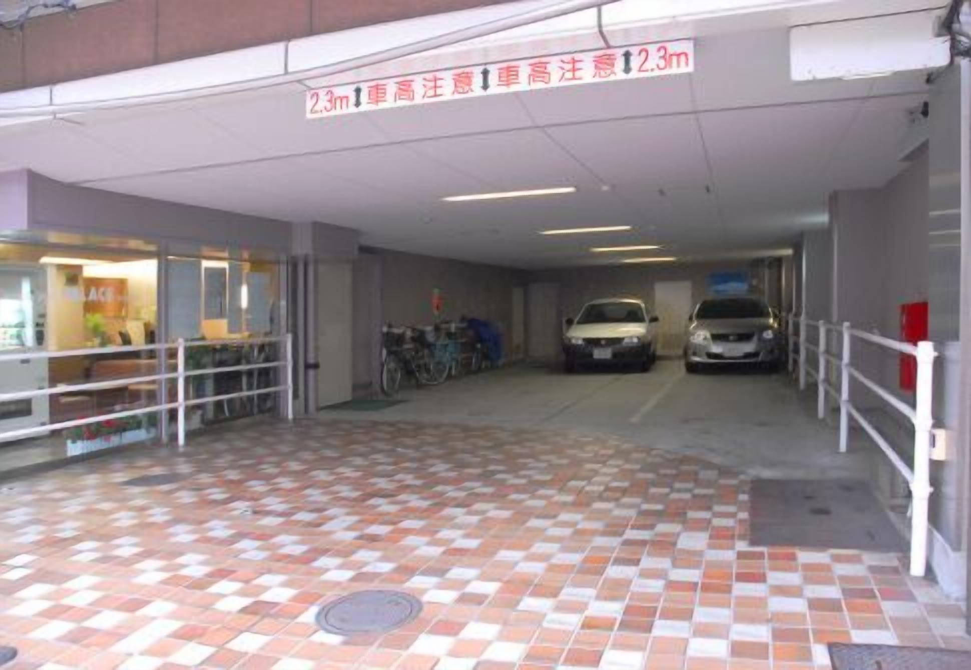 Ingang van een parkeergarage met betegelde vloer, een bord met maximale hoogte en twee geparkeerde auto's.