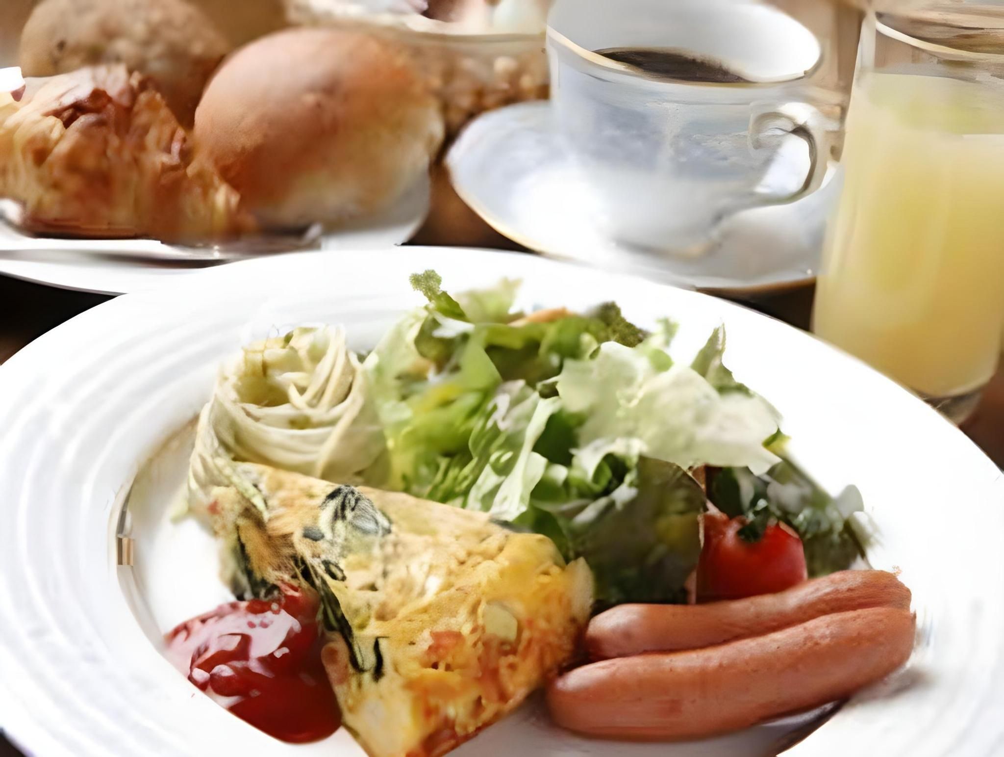 Un piatto con un'insalata, una fetta di quiche, salsicce e ketchup.