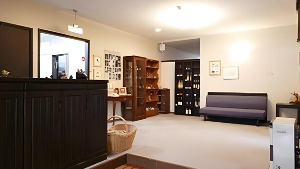 A spacious room with a large wooden cabinet, a sofa, and a collection of framed pictures on the wall. - Guest House Hilltop (Nagano)