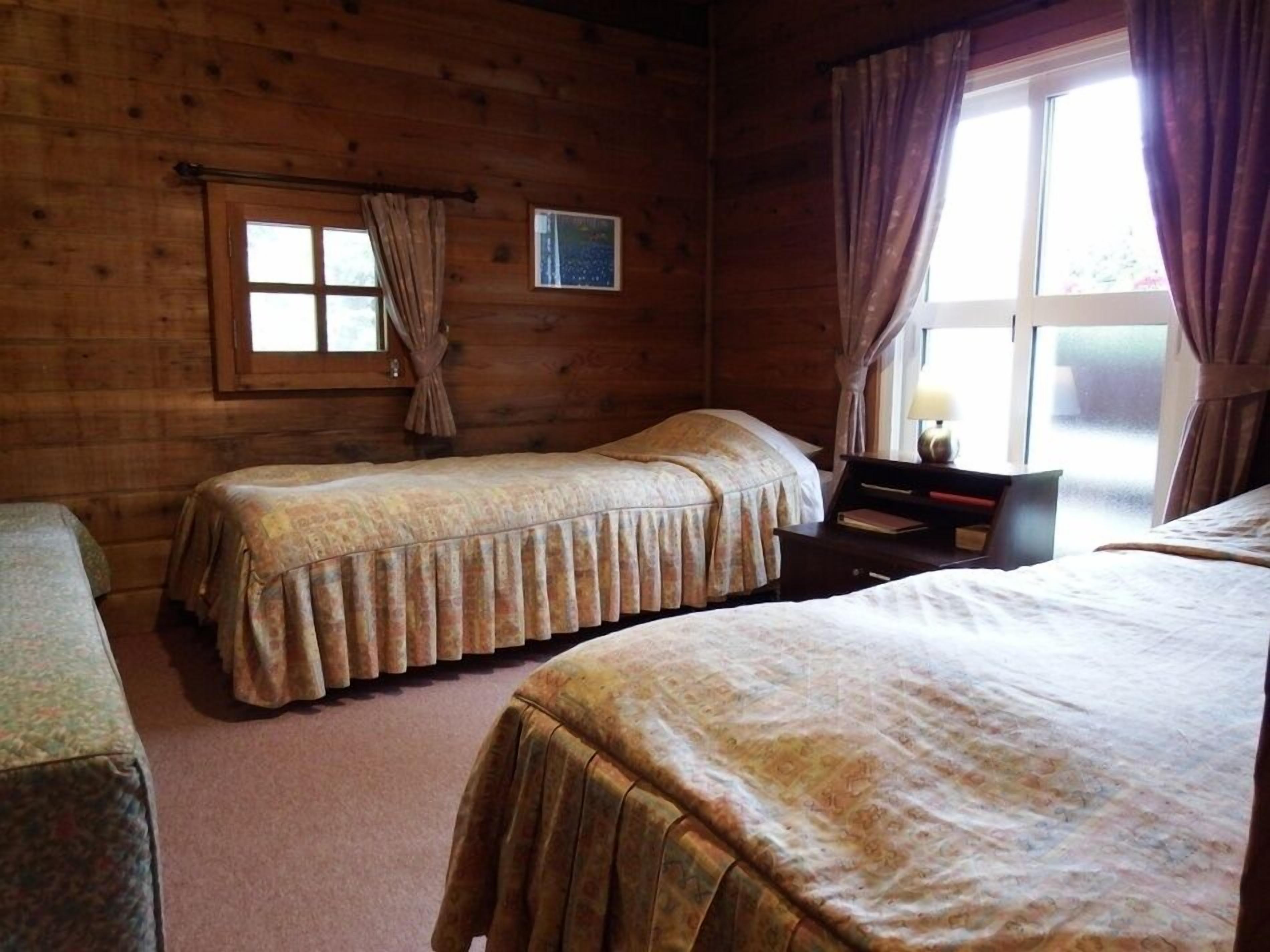 A wooden cabin room with two beds, a small table, and a window with curtains.