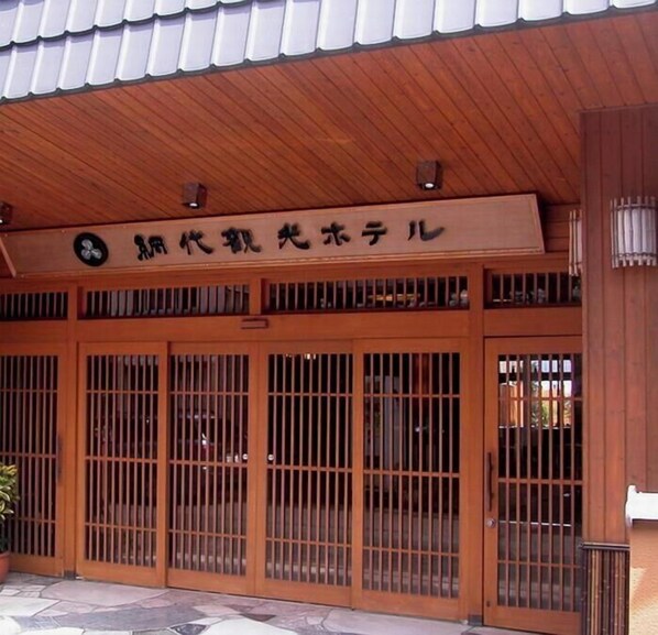 A traditional Japanese building with a tiled roof, wooden doors with vertical bars, and a sign with Japanese characters. - Ajiro Kanko Hotel (Atami)