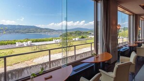 A room with large windows overlooking a scenic view of a lake and mountains. There are several chairs and tables arranged for dining or sitting. - Wano Resort Hazu (Gamagori)