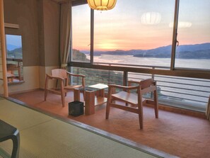 A room with a view of a sunset over a river, wooden furniture, and a large window. - Wano Resort Hazu (Gamagori)