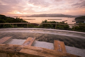 A hot spring with wooden seating and a view of a lake and mountains during sunset. - Wano Resort Hazu (Gamagori)