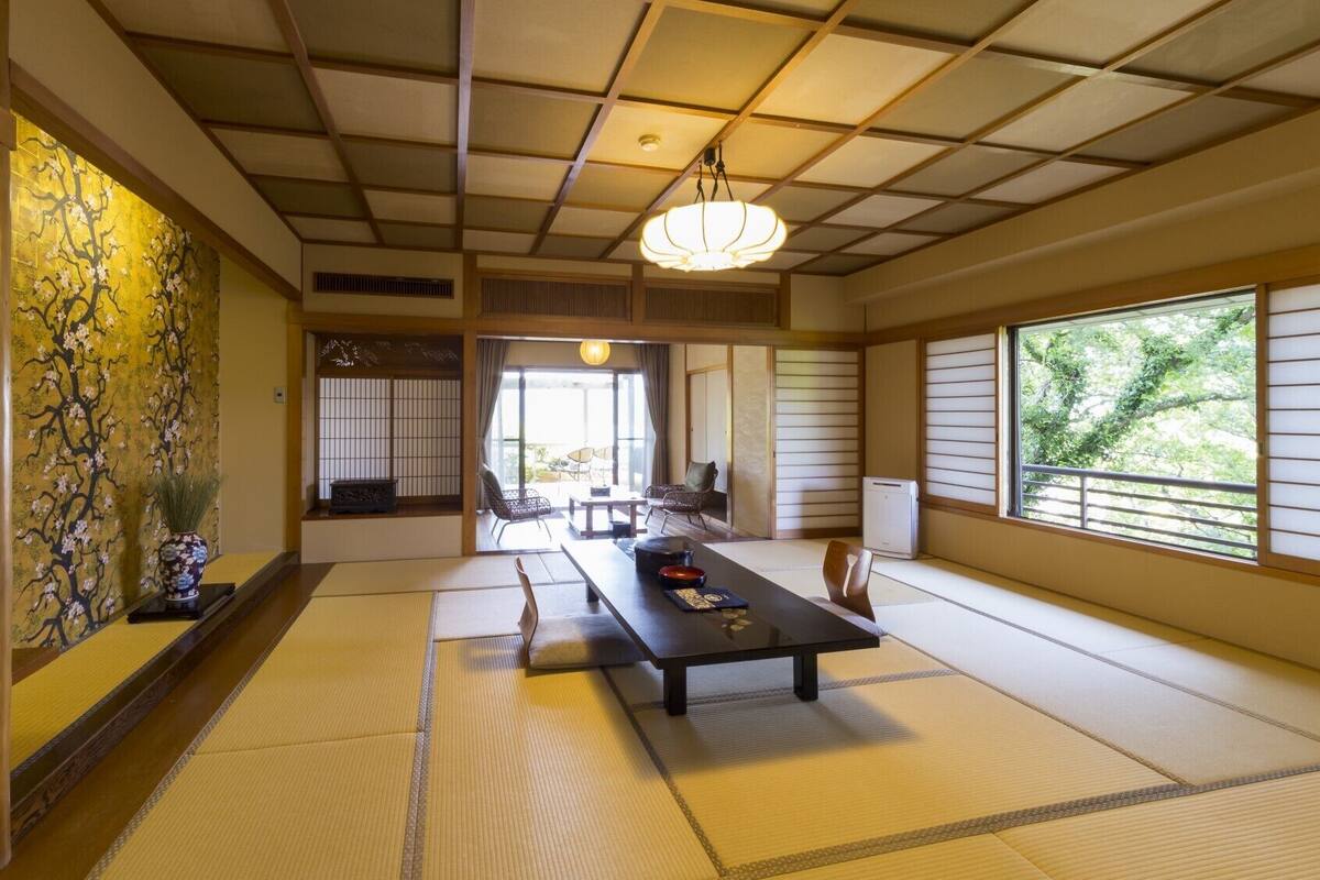 Ein traditioneller japanischer Raum mit Tatami-Böden, einem niedrigen Tisch, Stühlen und Blick durch einen Shoji-Bildschirm.