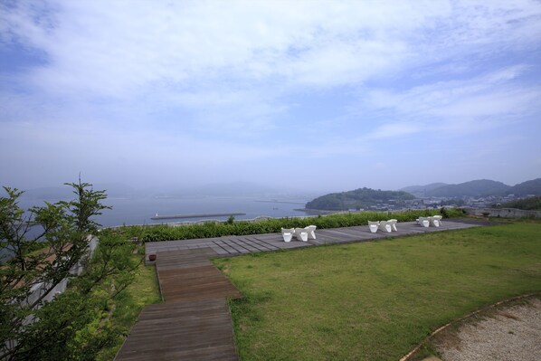 A view of a coastal area with a wooden deck, white outdoor furniture, and a grassy lawn.