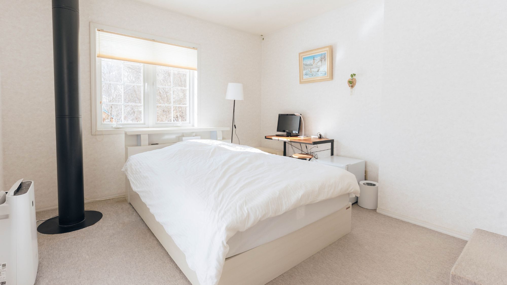 A bedroom with a bed, a desk with a computer, a lamp, a window, and a radiator.