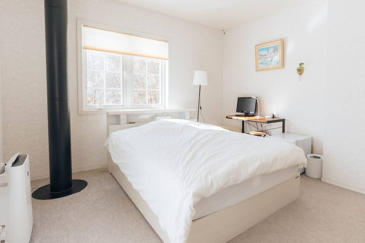 Une chambre à coucher avec un lit, un bureau avec un ordinateur, une lampe, une fenêtre et un radiateur.