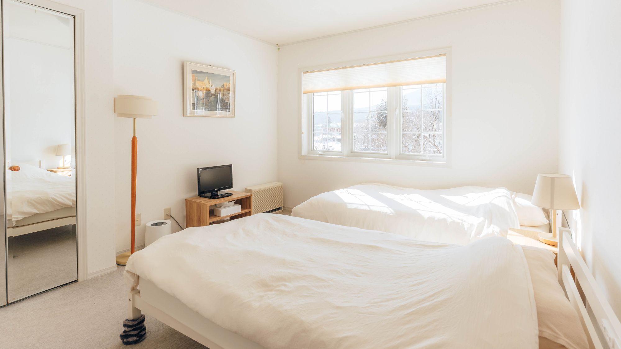 A hotel room with two beds, a television, a mirror, a window with a view, and a picture on the wall.