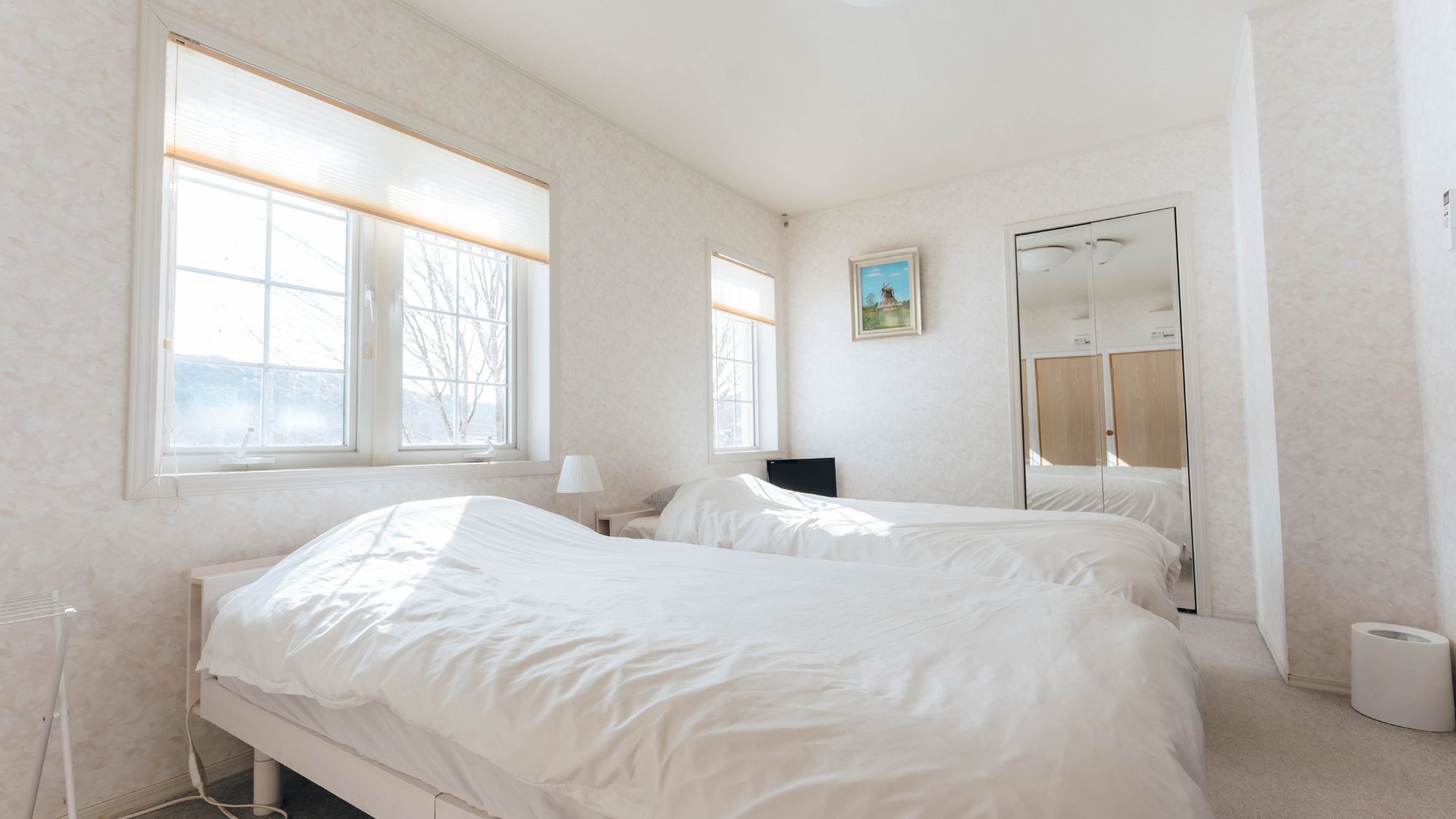 Une chambre avec deux lits, de grandes fenêtres, un tableau et un miroir.