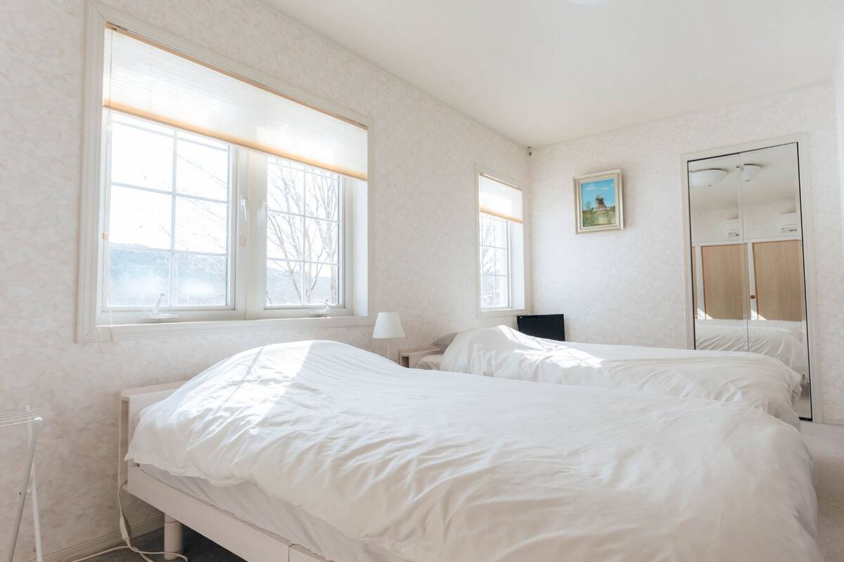 Une chambre avec deux lits, de grandes fenêtres, un tableau et un miroir.