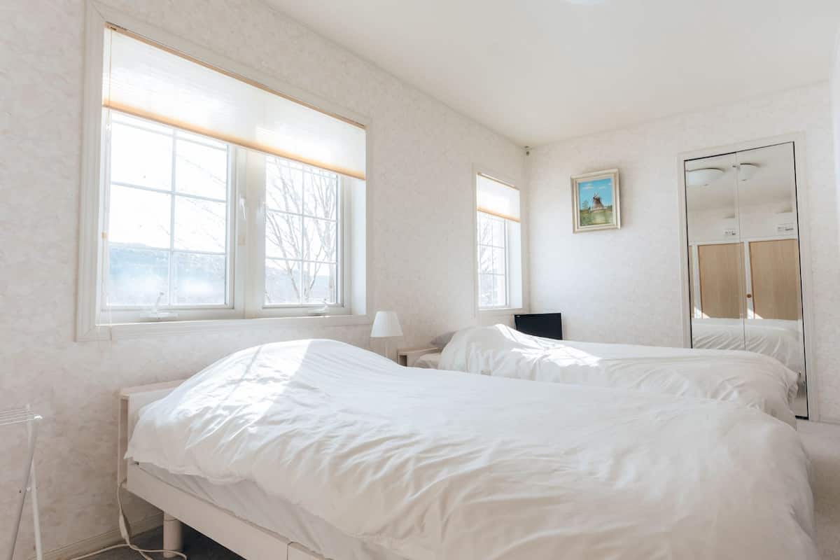 Ein Schlafzimmer mit zwei Betten, großen Fenstern, einem Gemälde und einem Spiegel.