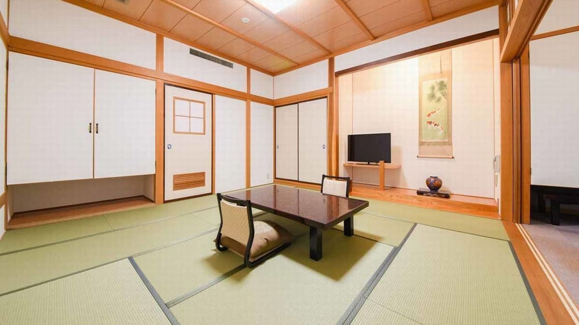 Une pièce de style japonais traditionnel, avec un sol recouvert de tatamis, une table basse, des portes coulissantes et un téléviseur.