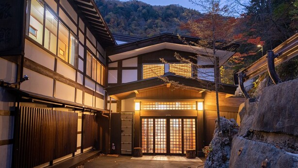 A traditional Japanese building with a wooden facade, a tiled entrance, and a stone pathway leading to the door. - Tsuruya Ryokan (Matsumoto)