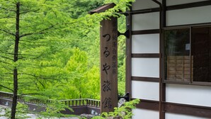A traditional Japanese building with a wooden signboard displaying Japanese characters. - Tsuruya Ryokan (Matsumoto)