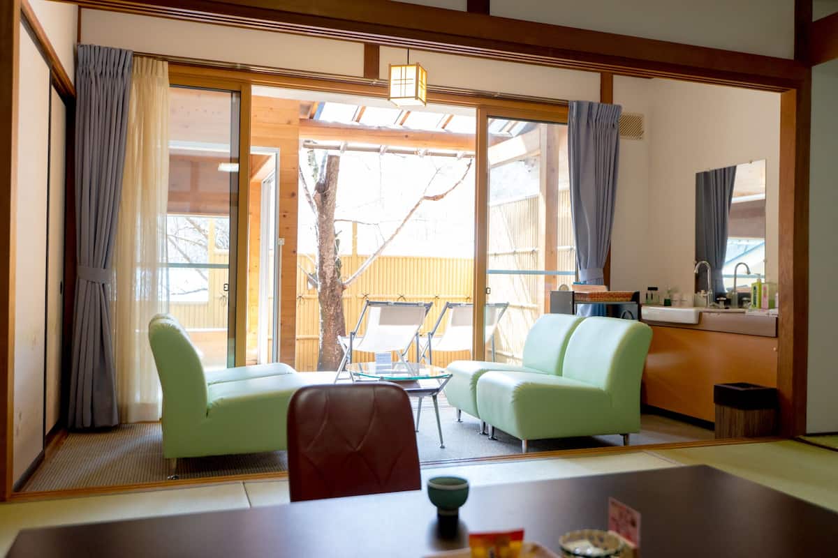 Una habitación con una mesa de comedor, dos sofás verdes, una mesita con un bol y vistas al exterior a través de amplios ventanales correderas.