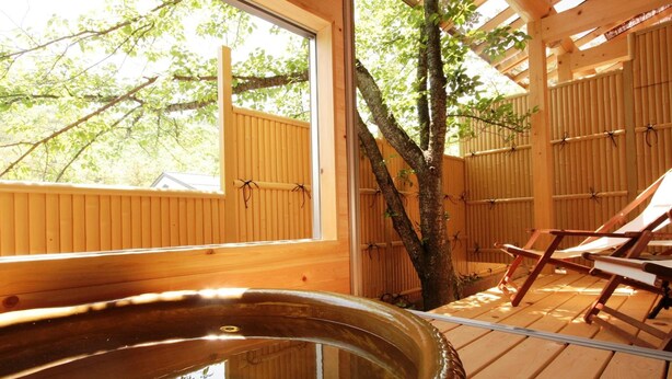 Una terraza de madera con un jacuzzi, paredes de madera y un árbol.