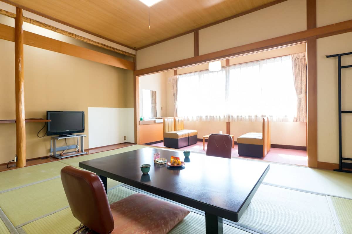 Una habitación tradicional japonesa con suelo de tatami, una mesa baja, un televisor y un sofá.