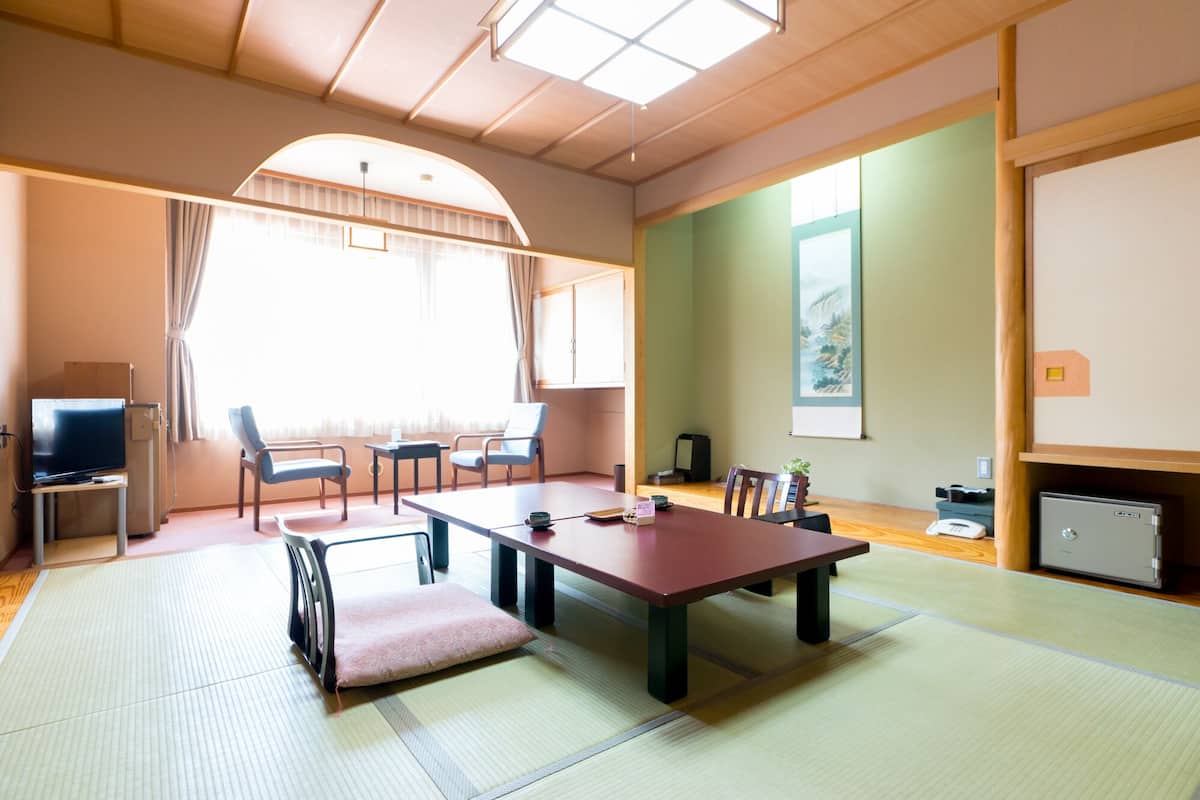 Una habitación japonesa tradicional con suelo de tatami, una mesa baja, sillas, un televisor y un cuadro en la pared.
