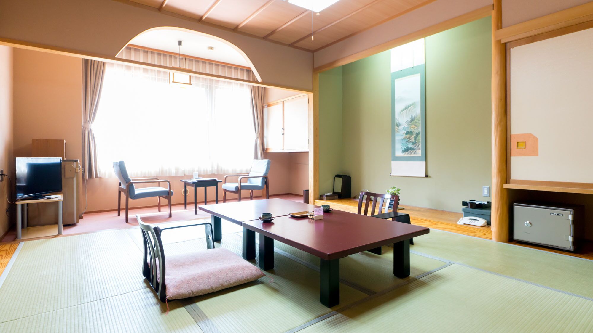 A room with tatami flooring, a low table, chairs, a television, and a painting on the wall.
