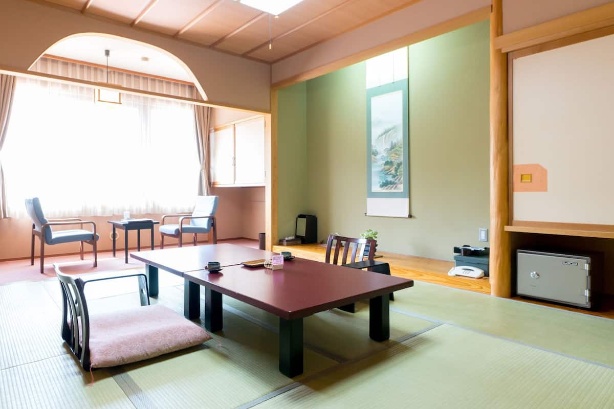 Una habitación con suelo de tatami, una mesa baja, sillas, un televisor y un cuadro en la pared.