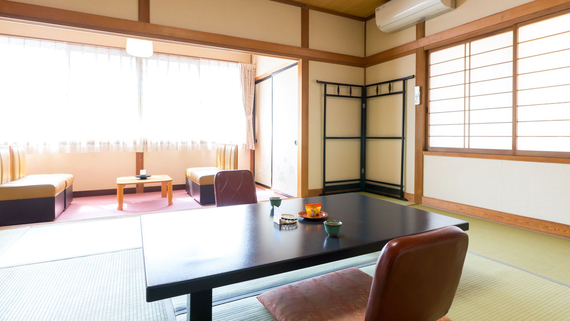 A tatami room with a low table, chairs, a sliding door, and a view of the outside.