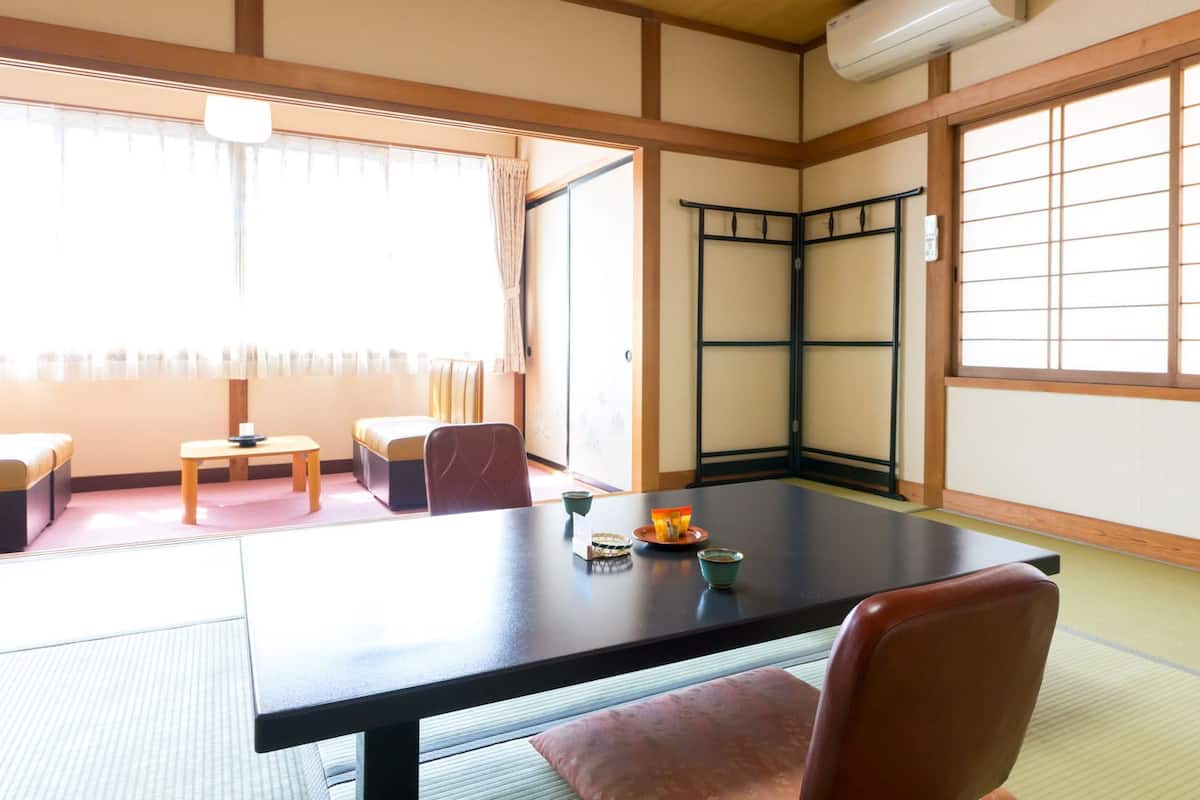 Una habitación de tatami con una mesa baja, sillas, una puerta corredera y vistas al exterior.