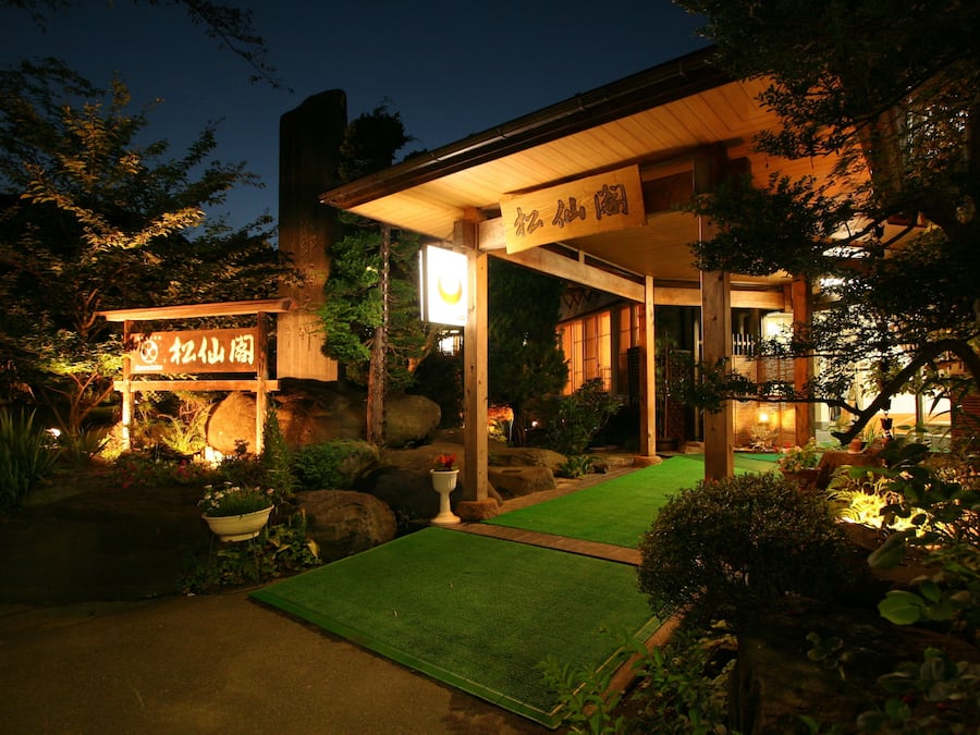 A traditional Japanese-style building with a wooden exterior and a green artificial turf pathway leading to the entrance.