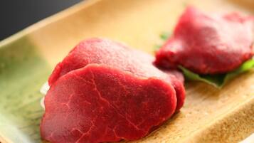 A close-up of a wooden table with a greenish hue, displaying two pieces of red meat, possibly steak, on a white plate with a green leaf garnish.