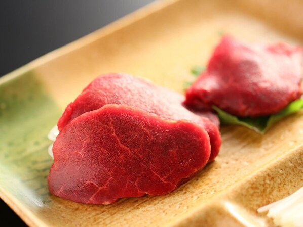 Primer plano de una mesa de madera con un tono verdoso, mostrando dos piezas de carne roja, posiblemente filete, sobre un plato blanco con una guarnición de hoja verde.