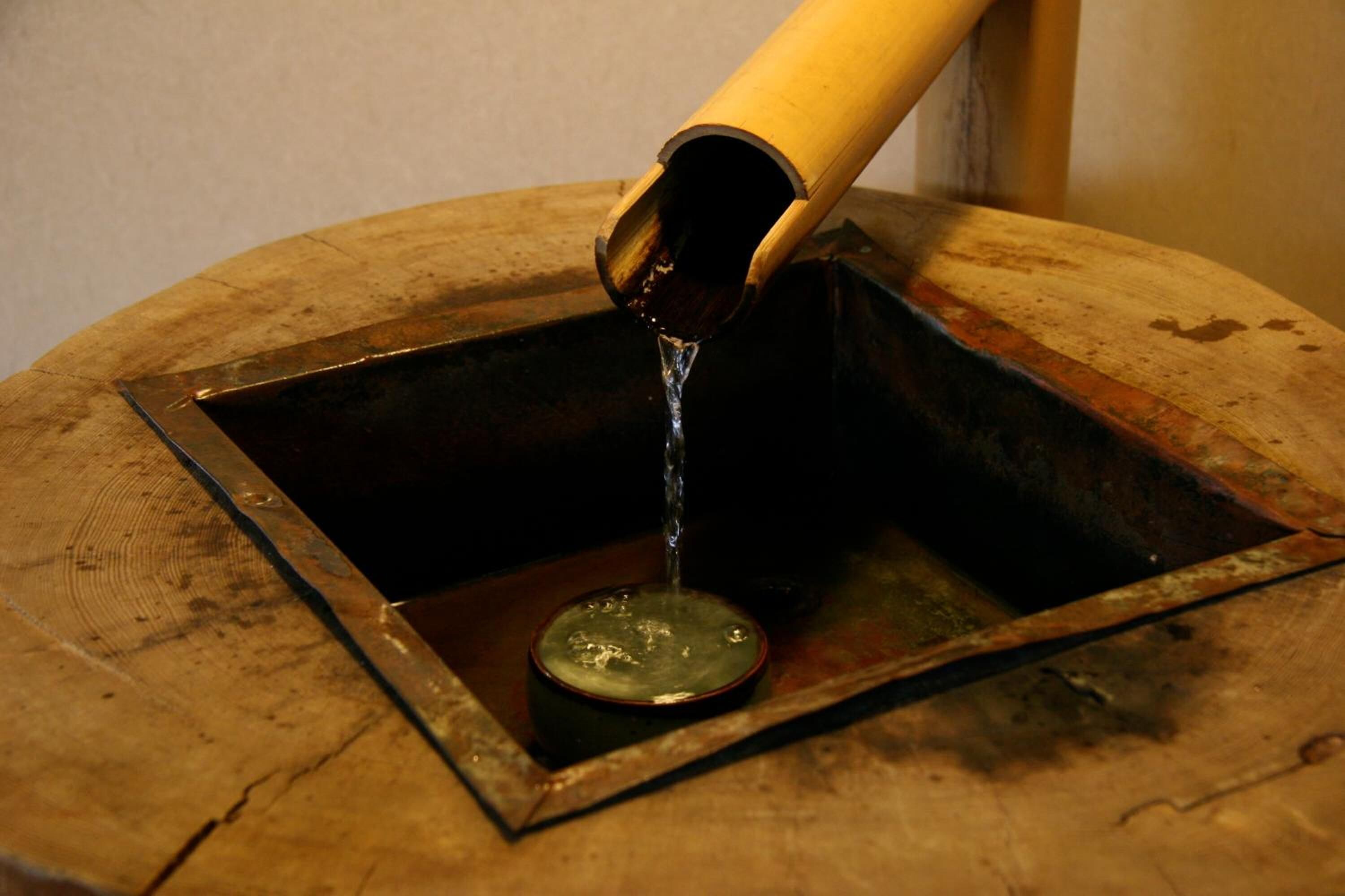 A metal basin with a wooden base and a bamboo spout pouring water into it.