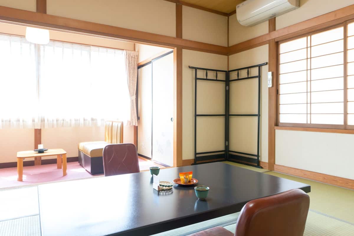 Una habitación japonesa tradicional con suelo de tatami, una mesa baja con cojín, una puerta corredera y una ventana con diseño de cuadrícula.