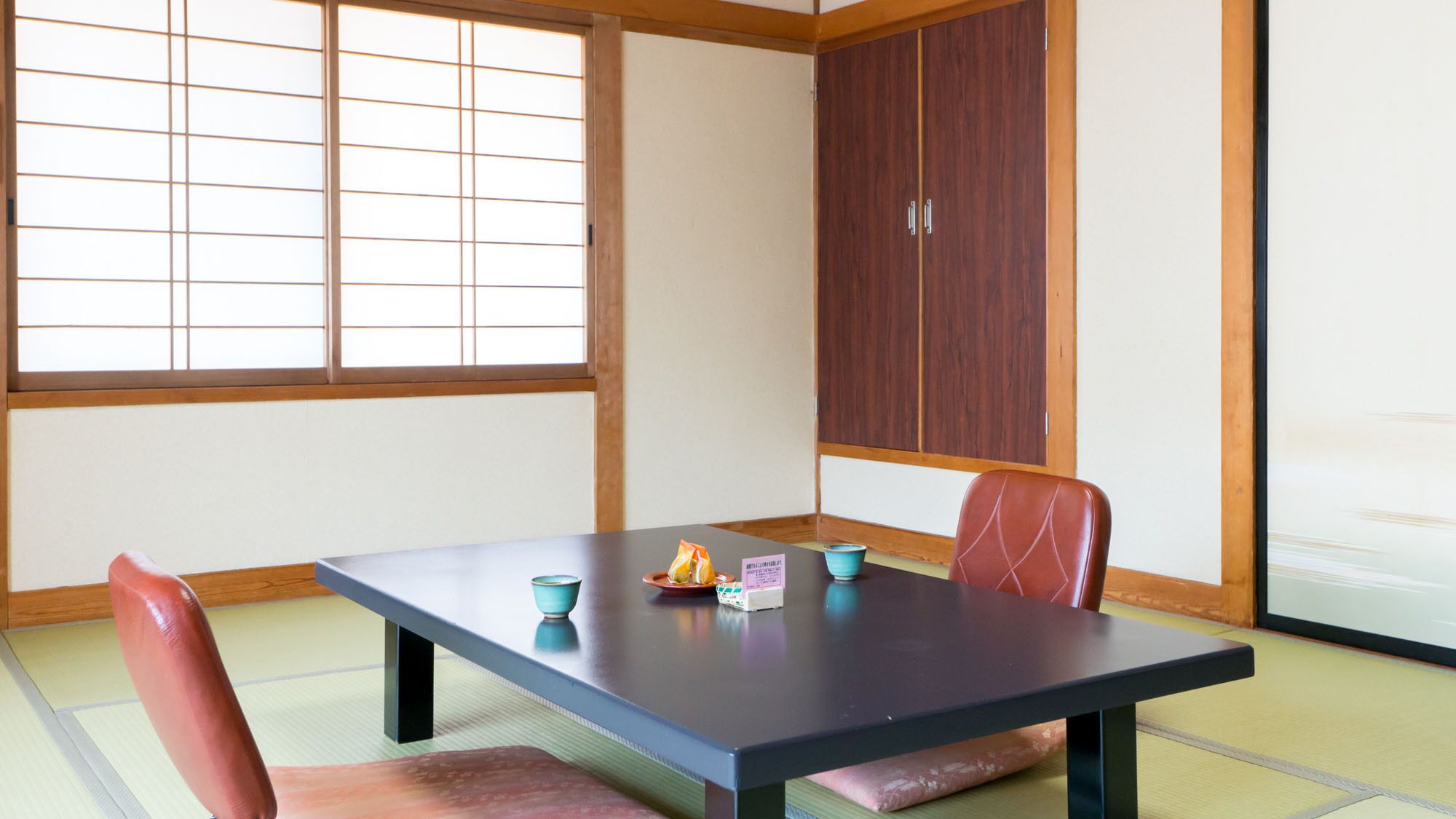 A traditional Japanese room with tatami flooring, a low table, and a sliding door.