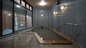 En stor inomhuspool med ett kaklat golv, en glasvägg och ett metallräcke.