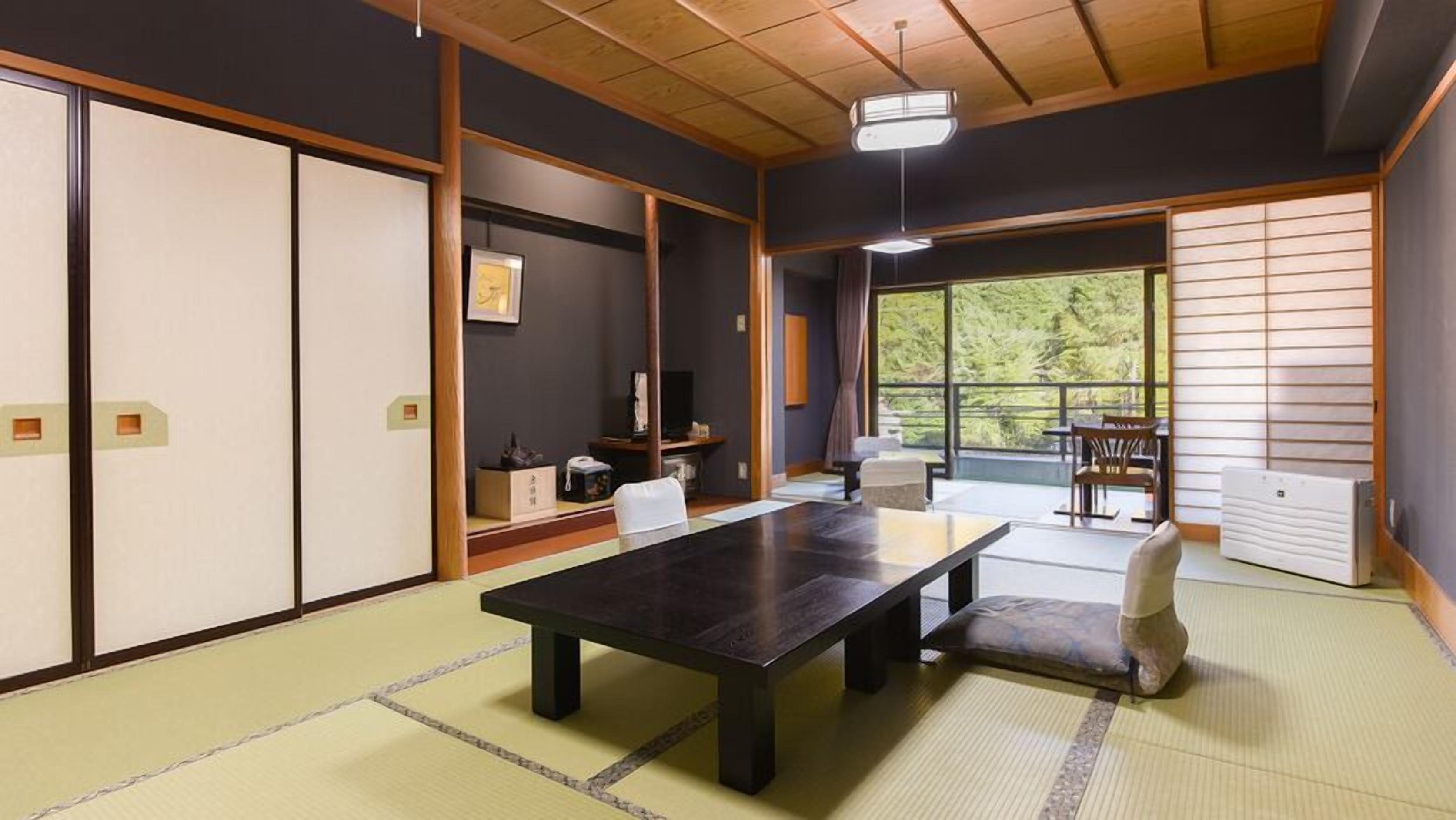 A traditional Japanese room with tatami flooring, a low table, a cushioned chair, sliding doors, and a view of greenery.