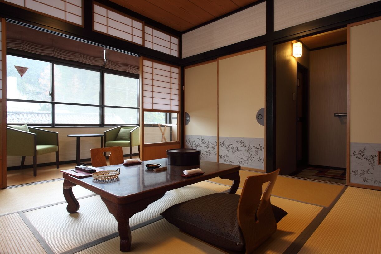 A traditional Japanese room with tatami flooring, a low table, chairs, and sliding doors.