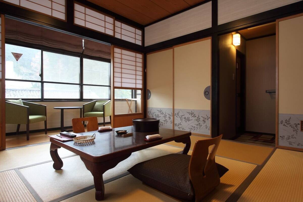 Ein traditioneller japanischer Raum mit Tatami-Böden, einem niedrigen Tisch, Stühlen und Schiebetüren.