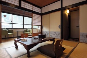 Una habitación japonesa tradicional con suelo de tatami, una mesita baja, sillas y puertas correderas.