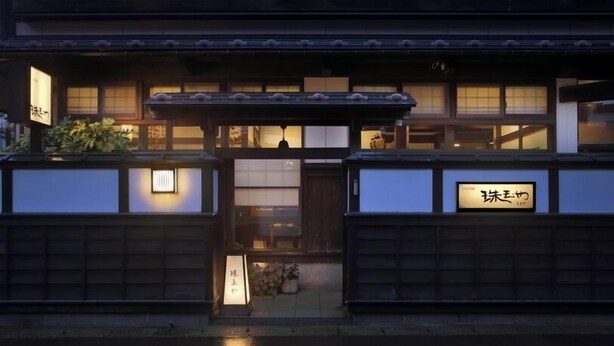 A traditional Japanese building with a wooden facade, a covered entrance, and illuminated signage. - Yutagawa Onsen Kuhe Ryokan Tamaya (Tsuruoka)