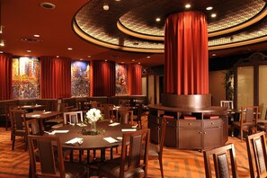 Un restaurante con mesas redondas, cortinas rojas y un techo decorativo.